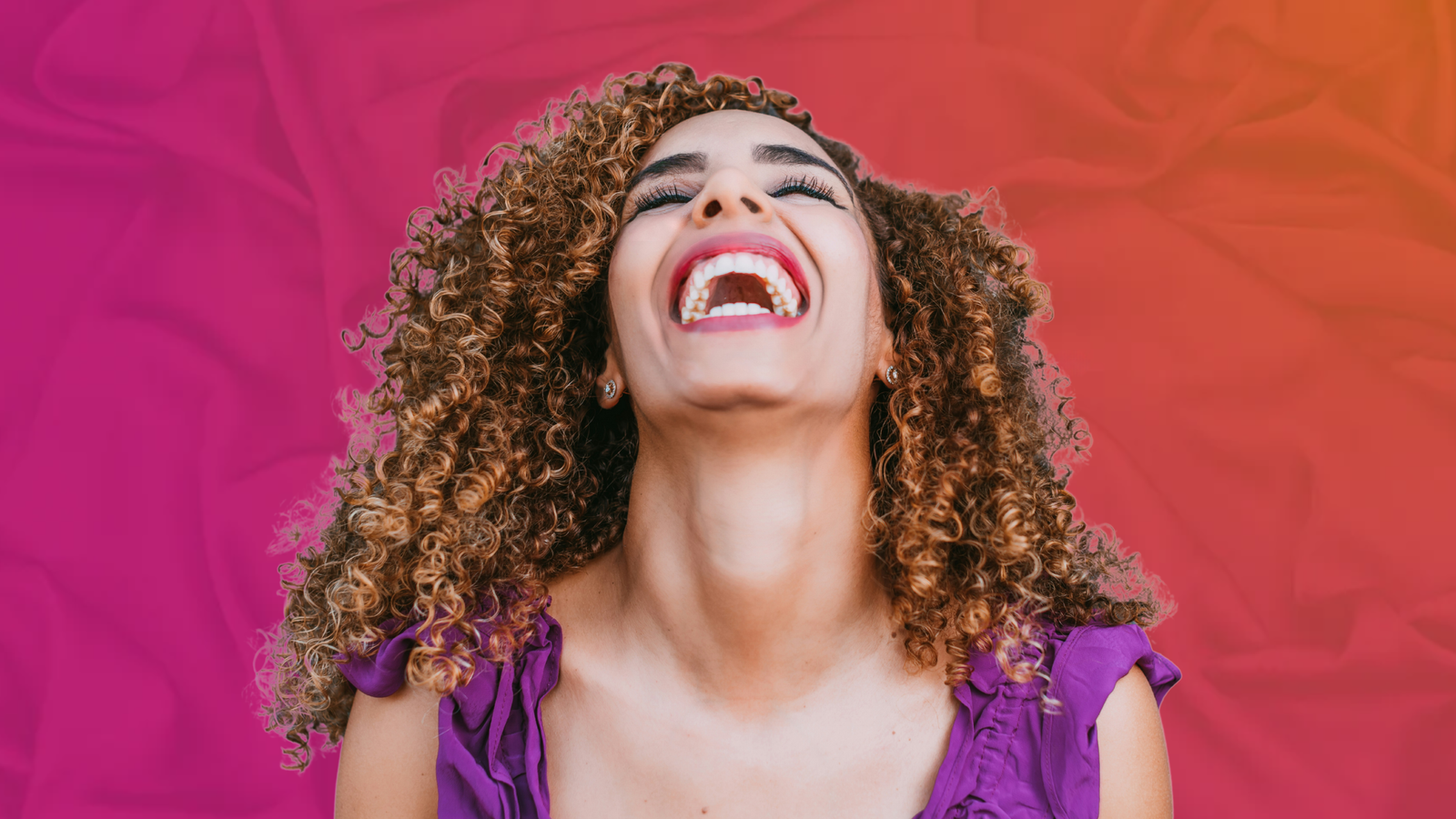 Woman smiling with eyes closed in a moment of bliss against a vibrant pink and orange background, representing intimacy, pleasure, and a truly Morgasmic Valentine’s Day.